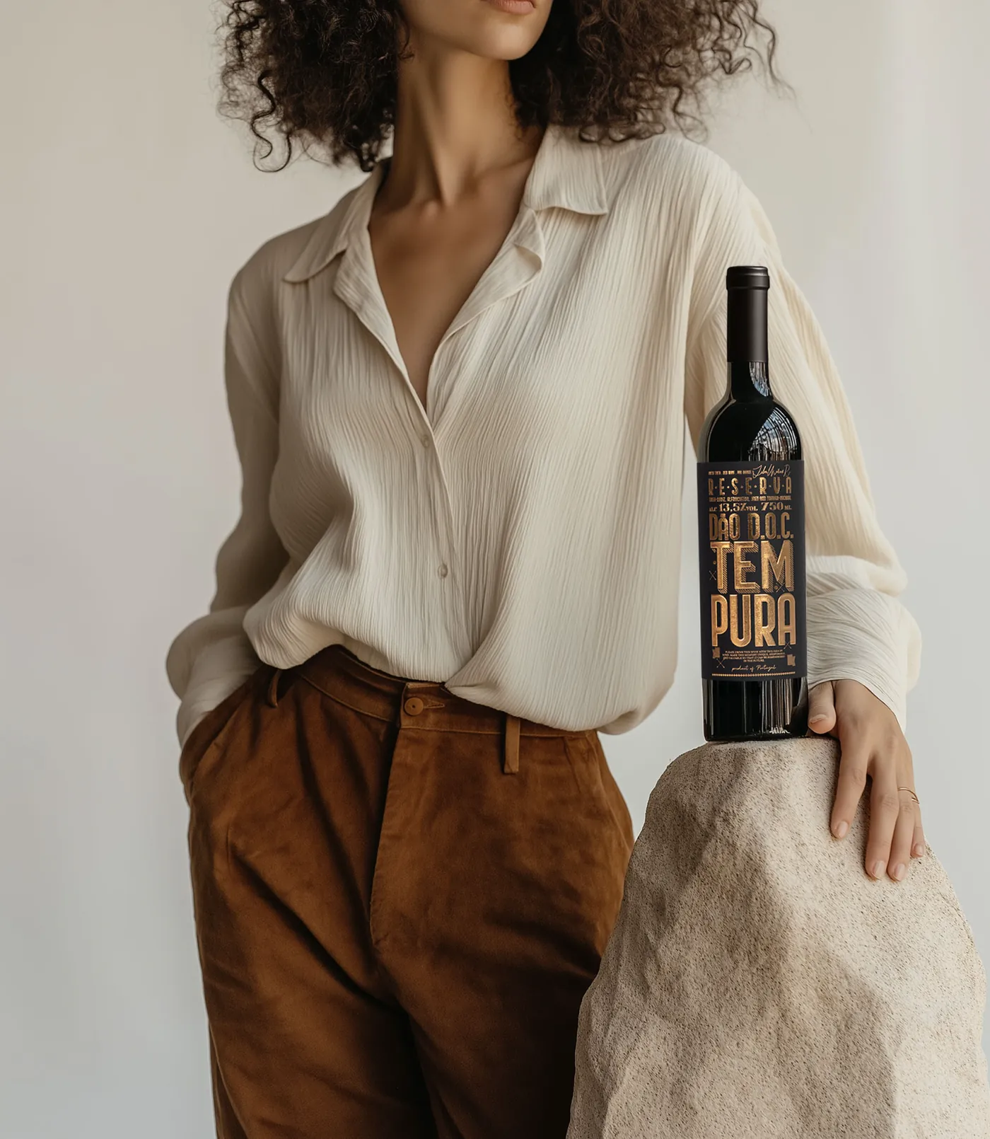 Modelo de camisa de linho e calças castanhas com a garrafa Tempura pousada numa pedra